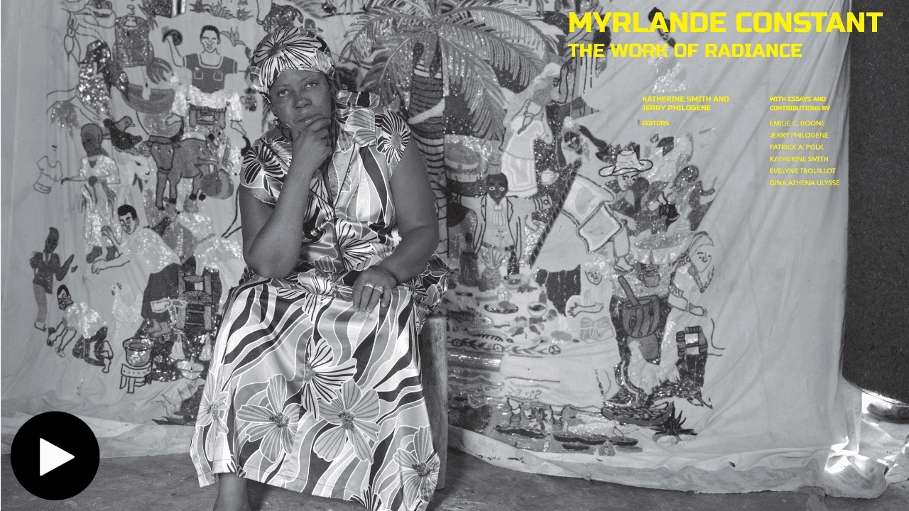 A black and white promotional photograph for "Myrlande Constant: The Work of Radiance," a past exhibition at the Fowler. Myrland sits in front of one of her artworks, one hand on her lap and the other on her chin. SHe wears a striped floral dress and a headwrap. 