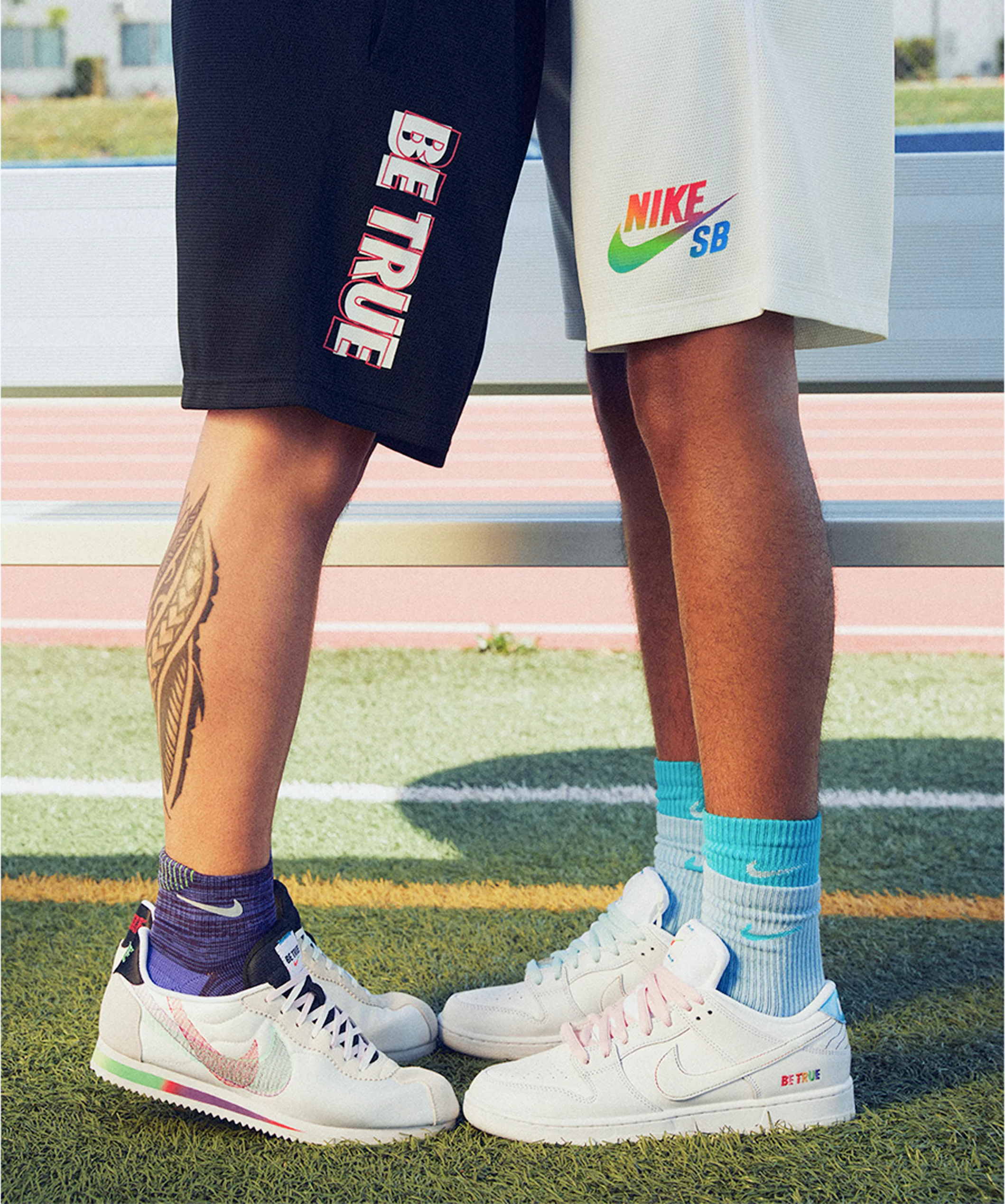Two people standing side by side wearing Nike SB "Be True" shorts and sneakers on a sports field