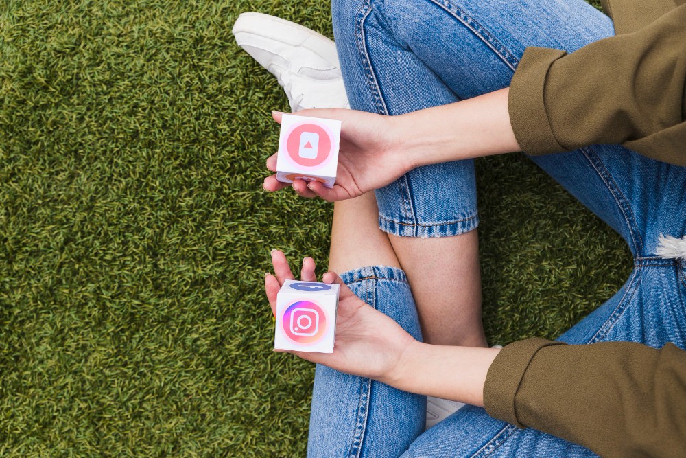 A woman sitting on green grass holding social media icons in hands