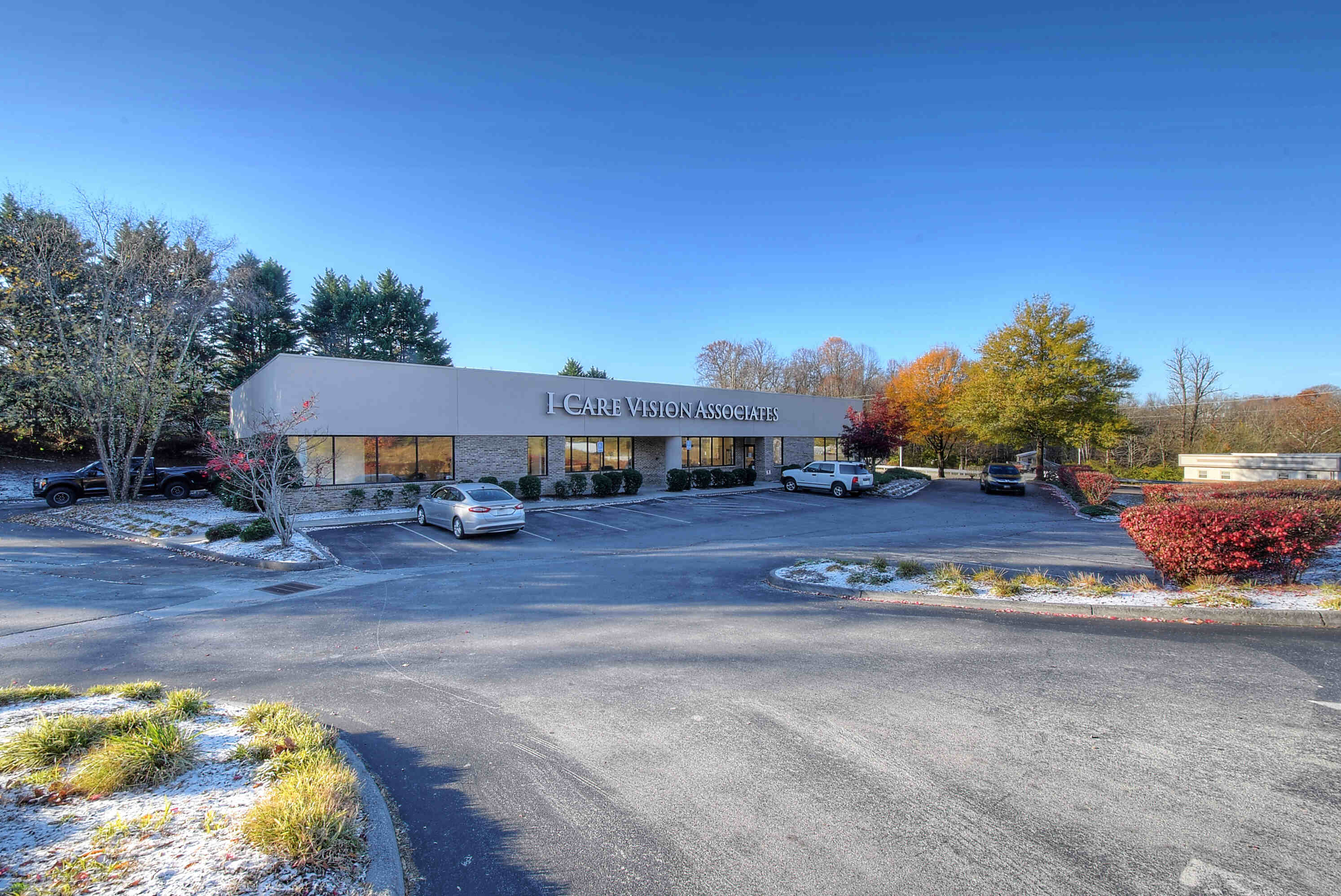 A parking lot with a building in the background, surrounded by trees and a clear blue sky.
