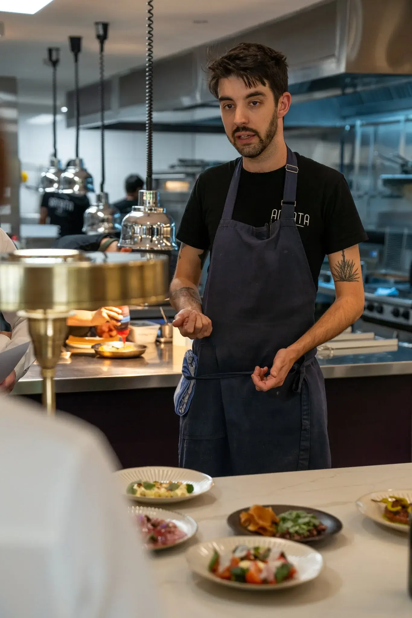 Annata chef presenting a row of tasting dishes at the open kitchen pass