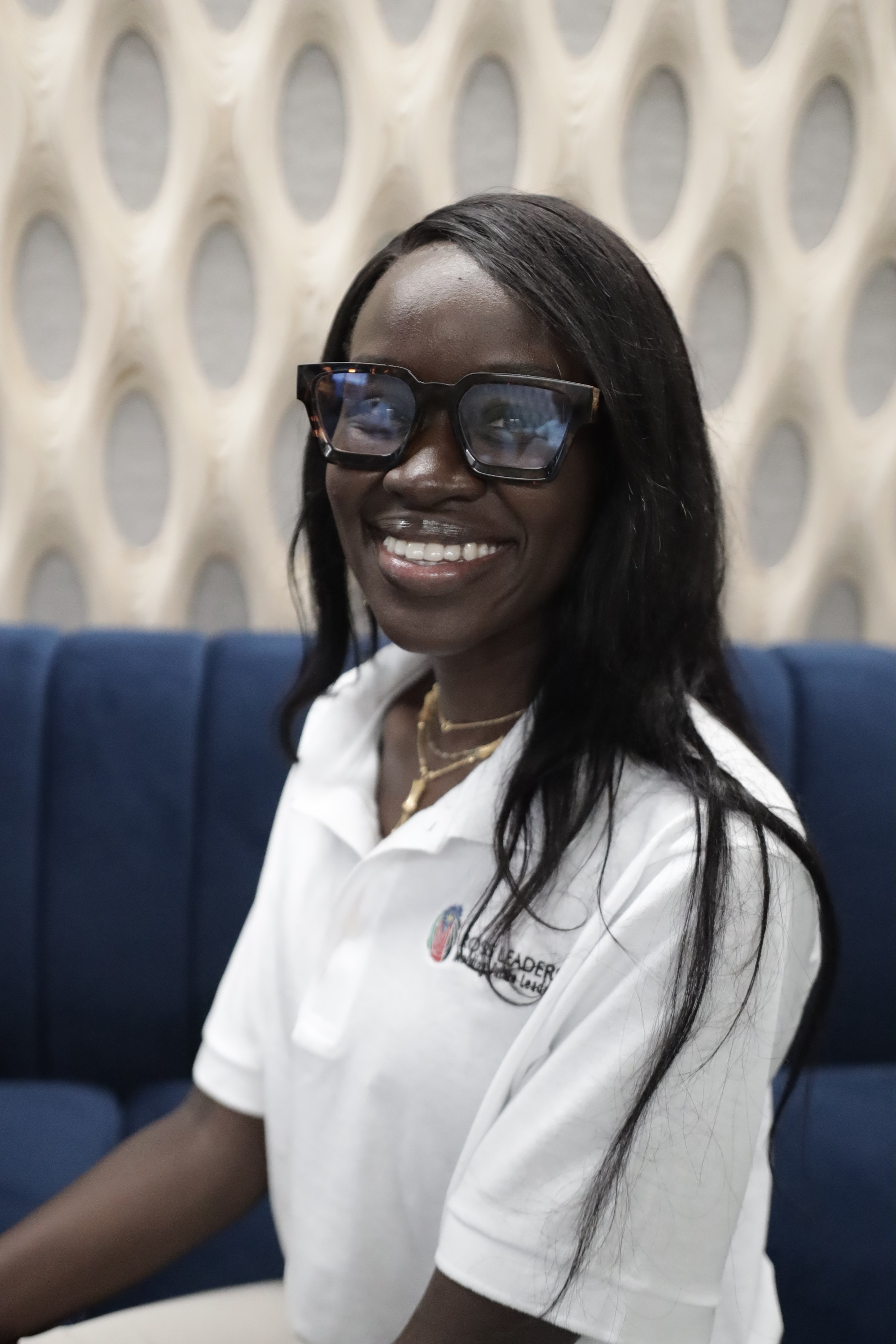 A young man in a formal outfit with a dark overcoat and rust-colored vest, gazing directly at the camera against a neutral background.