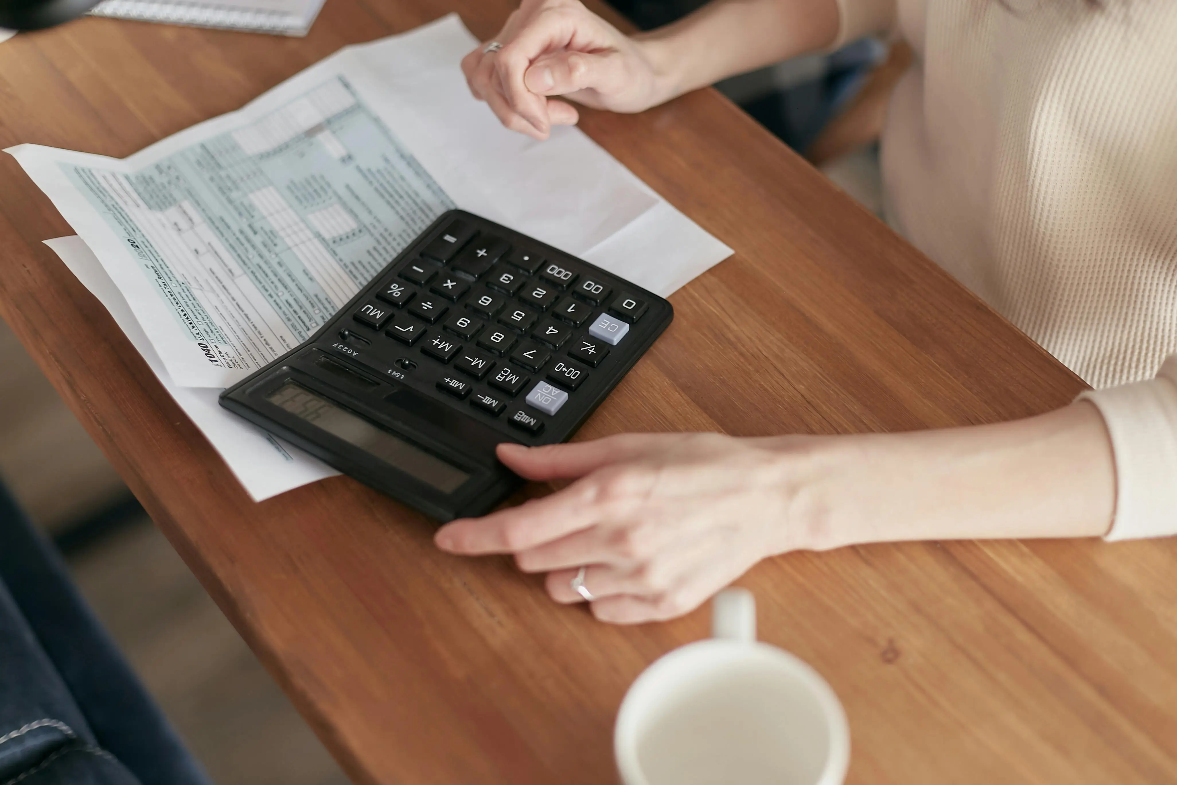Person using a calculator and reviewing financial documents at a wooden desk