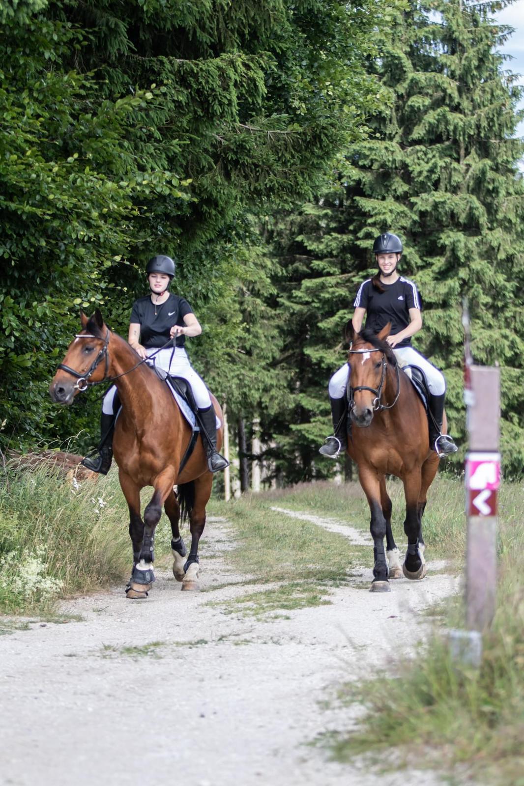 A smiling woman with her arms crossed, standing against a dark green background. She has long, dark hair.