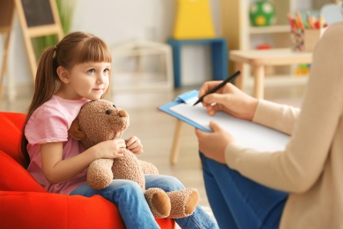 A child looking up at a counsellor, the child clutches a teddy bear 