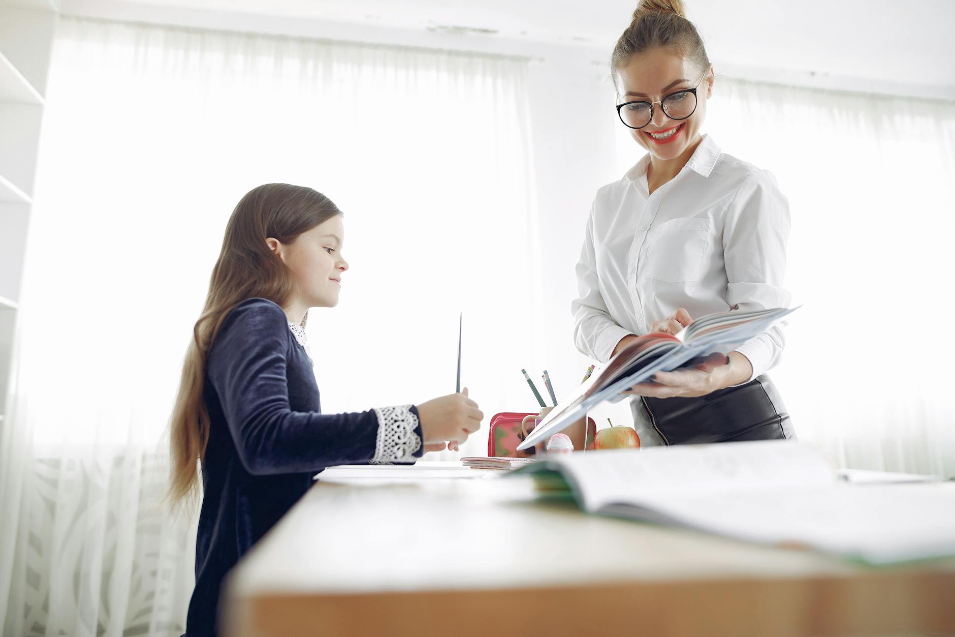 A good teacher kneels beside a primary student's desk to provide one-on-one guidance on a science project.
