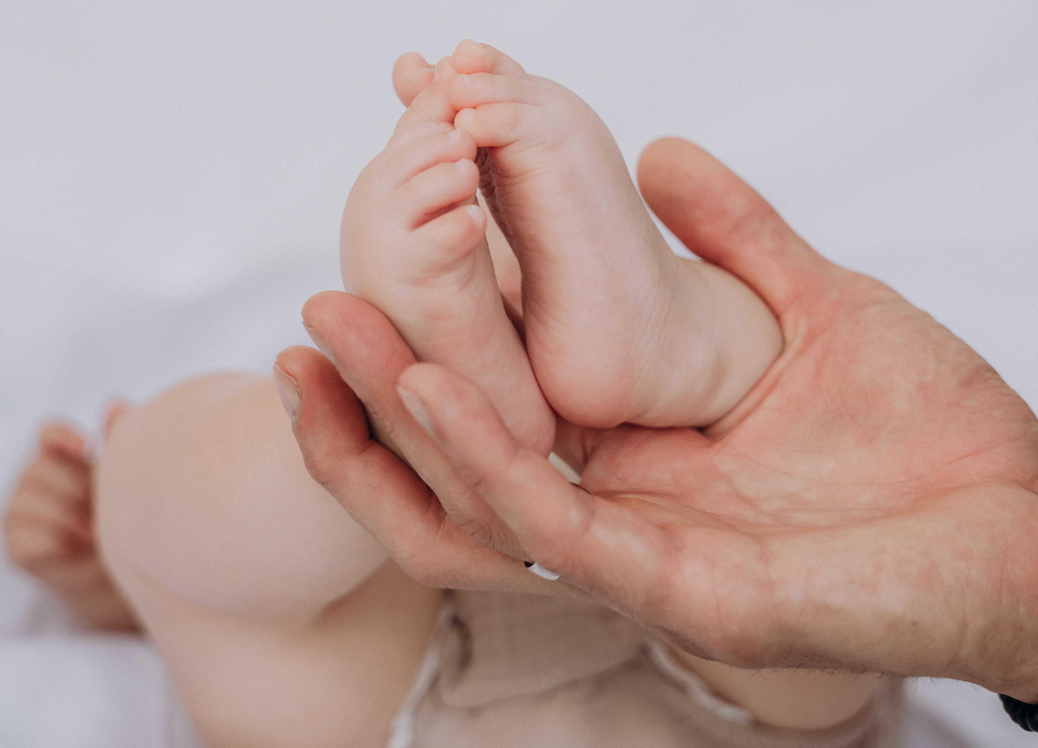 Neugeborenenfotografie in Bogen – Babyfüße in den Händen der Eltern bei natürlicher Babyfotografie.
