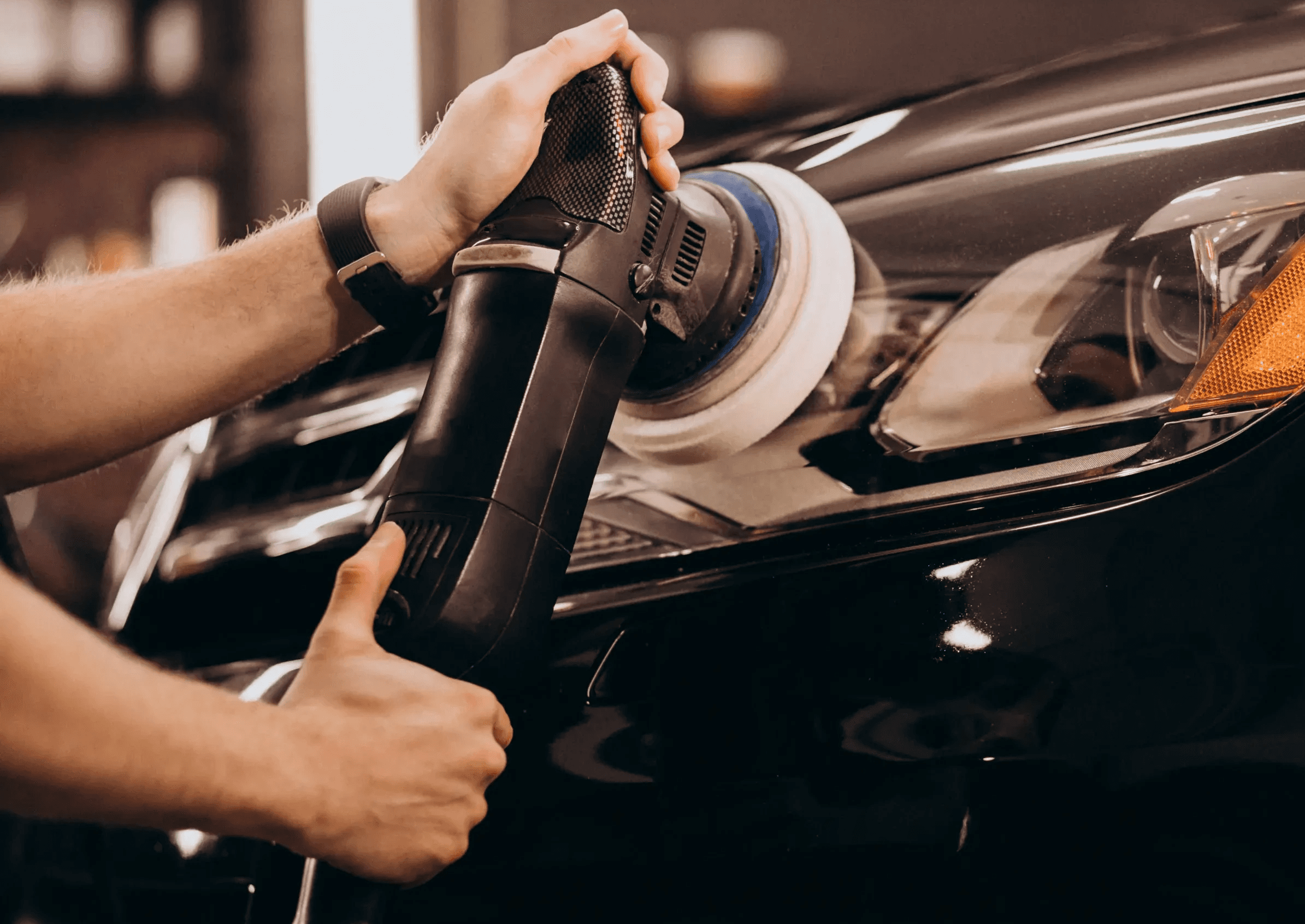 Close-up of a professional detailer in Houston using a dual-action orbital polisher for paint correction and scratch removal on a black luxury car.