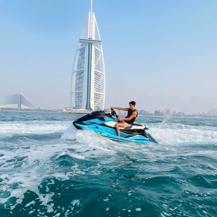 Man riding a blue Jet Ski with the Burj Al Arab tower in the background.