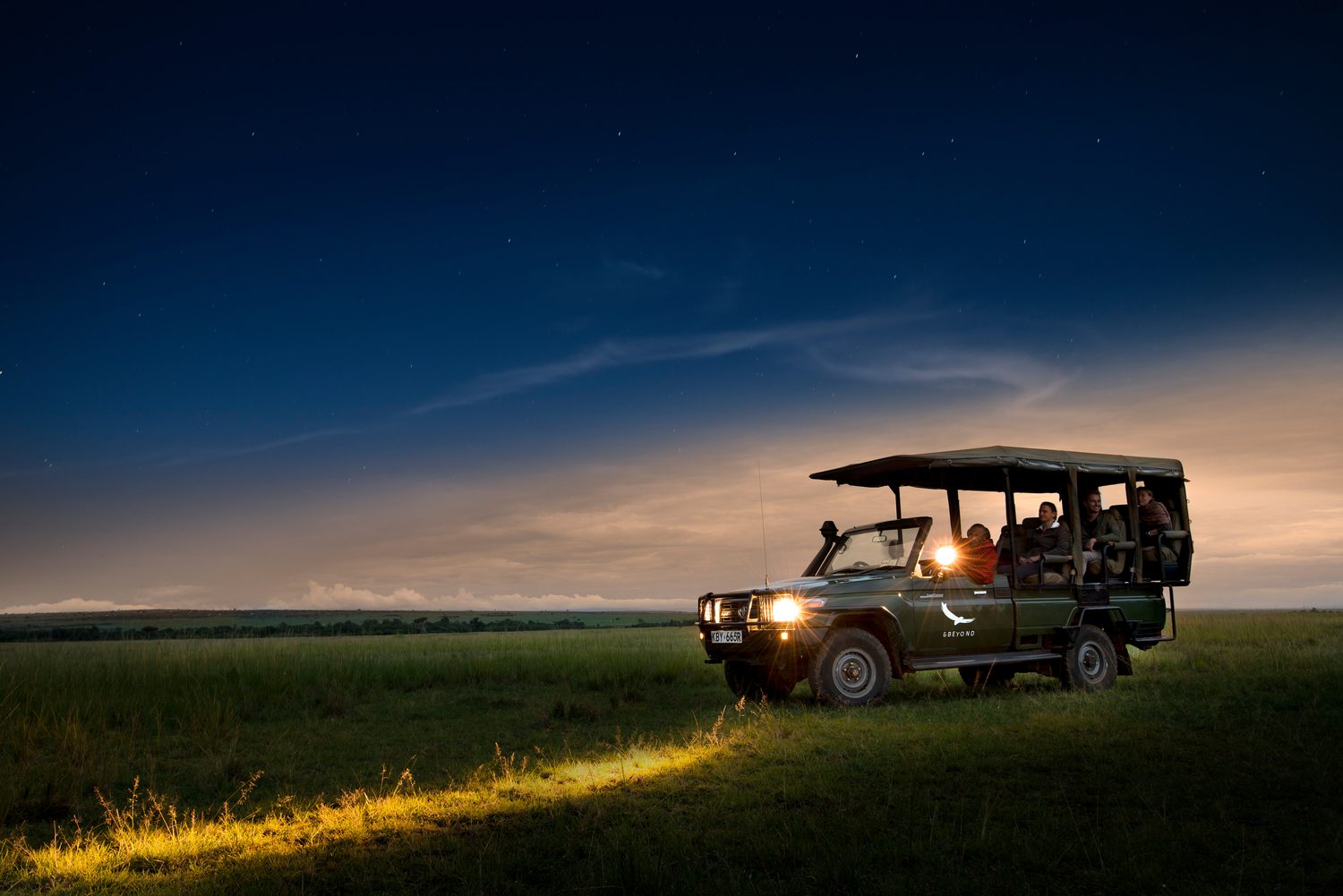A game-drive vehicle parked on open plains under a starlit sky, headlights glowing