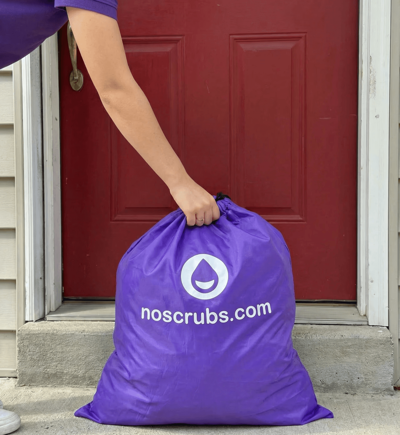 NoScrubs delivery partner collecting a purple laundry bag from a customer’s front door