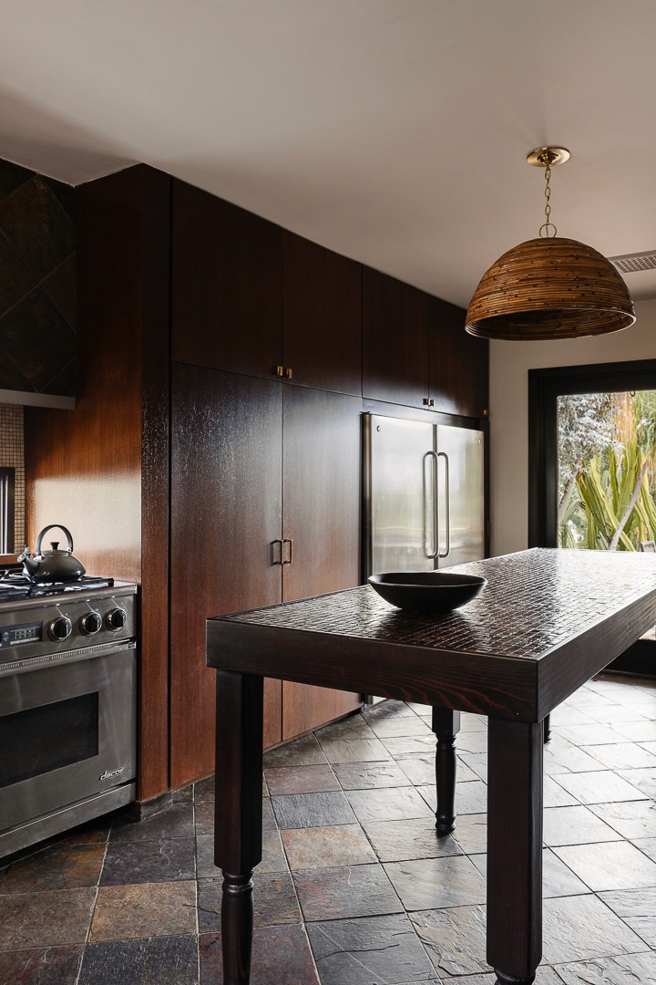 This luxurious interior features a limestone fireplace, timber accents, woven wooden chairs, and a natural wood coffee table, all unified by an earthy tonal palette