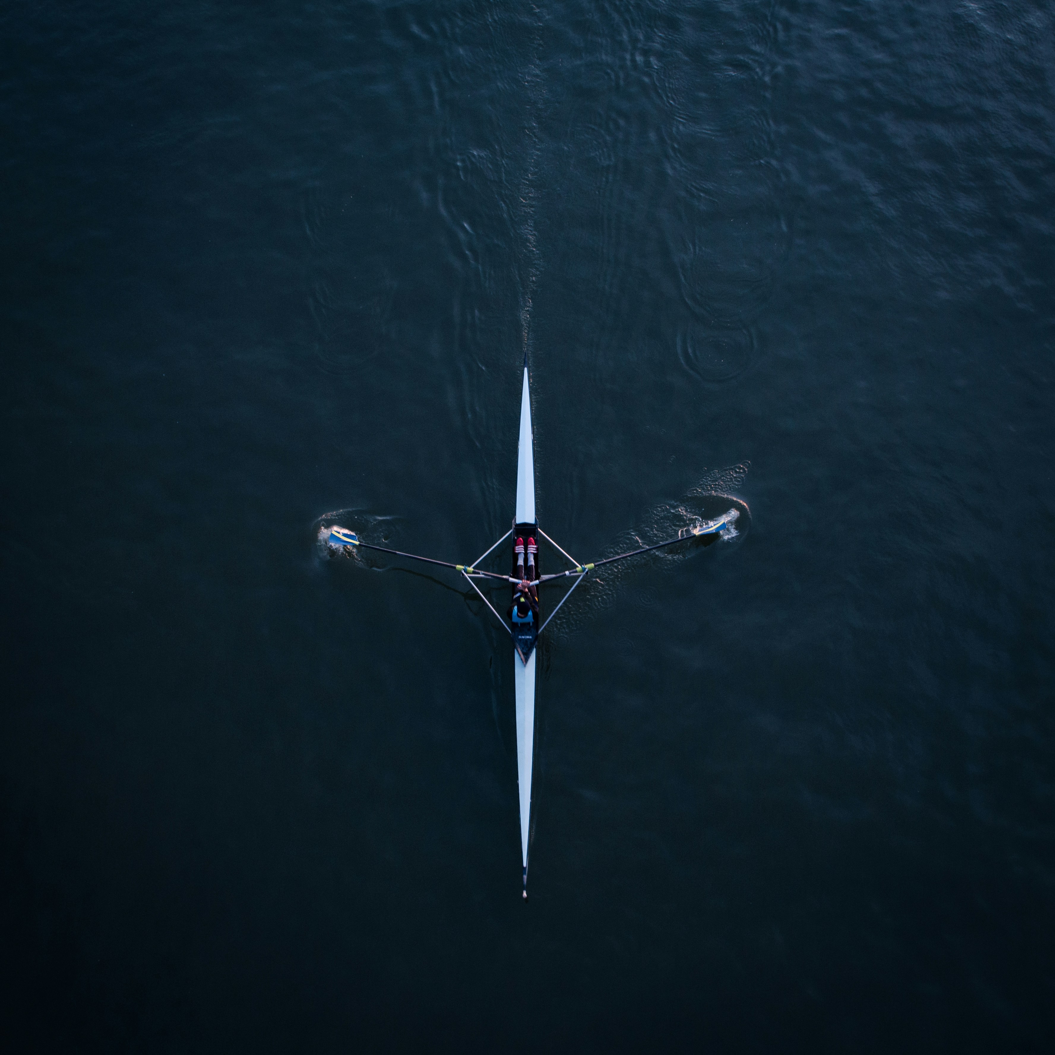 Smiling young woman with long hair standing against a dark green background, holding a finger to her chin.