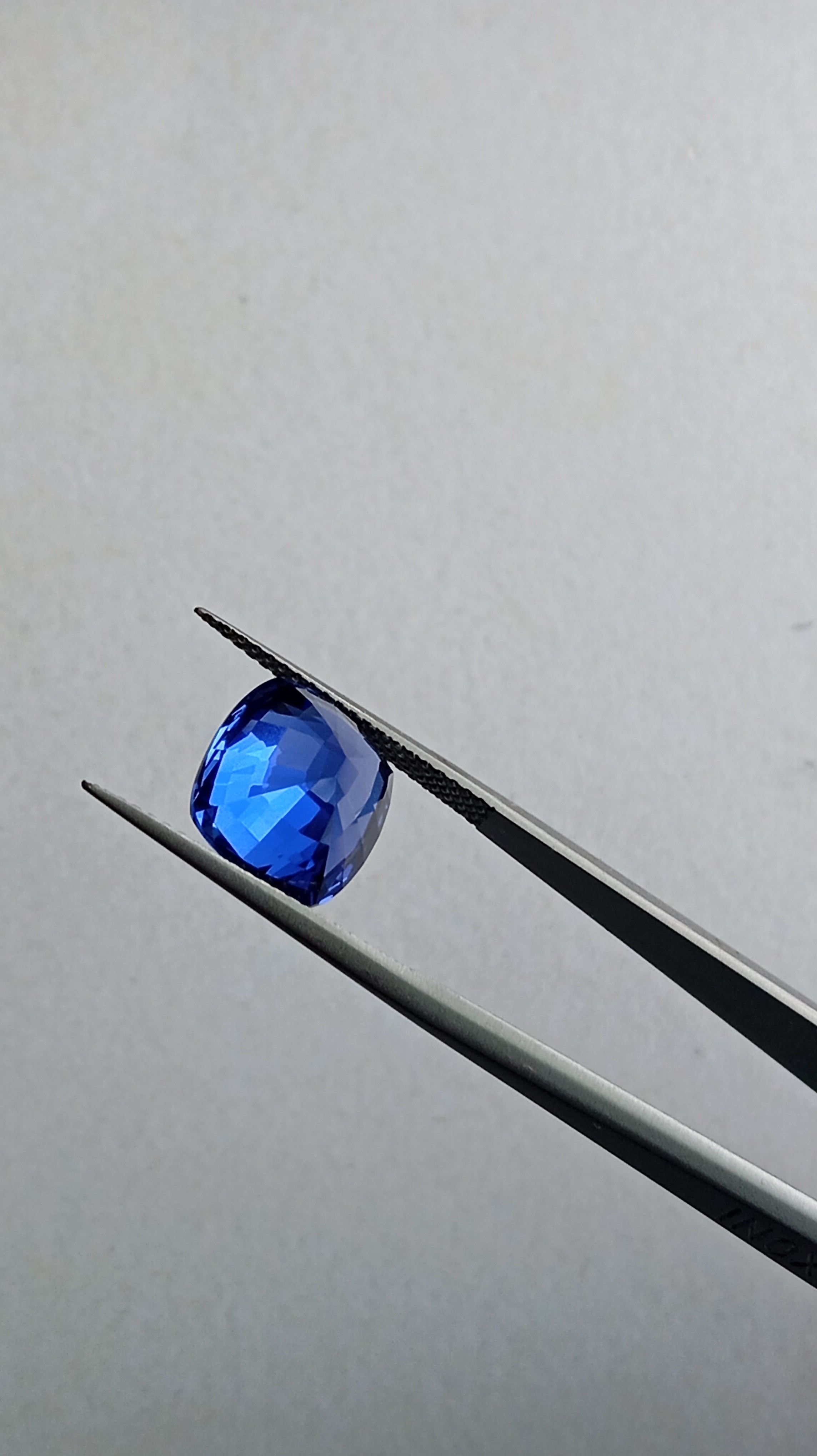 Back side view of a vivid royal blue heart-shaped lab-grown sapphire gemstone held in tweezers for scale.