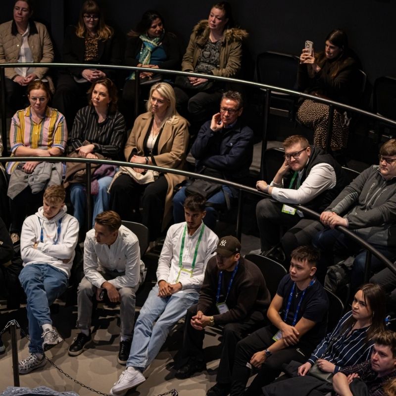 A diverse group of attendees seated in a tiered showroom, attentively listening to a presentation during an Innovation Week event at Lava Show in Reykjavík.