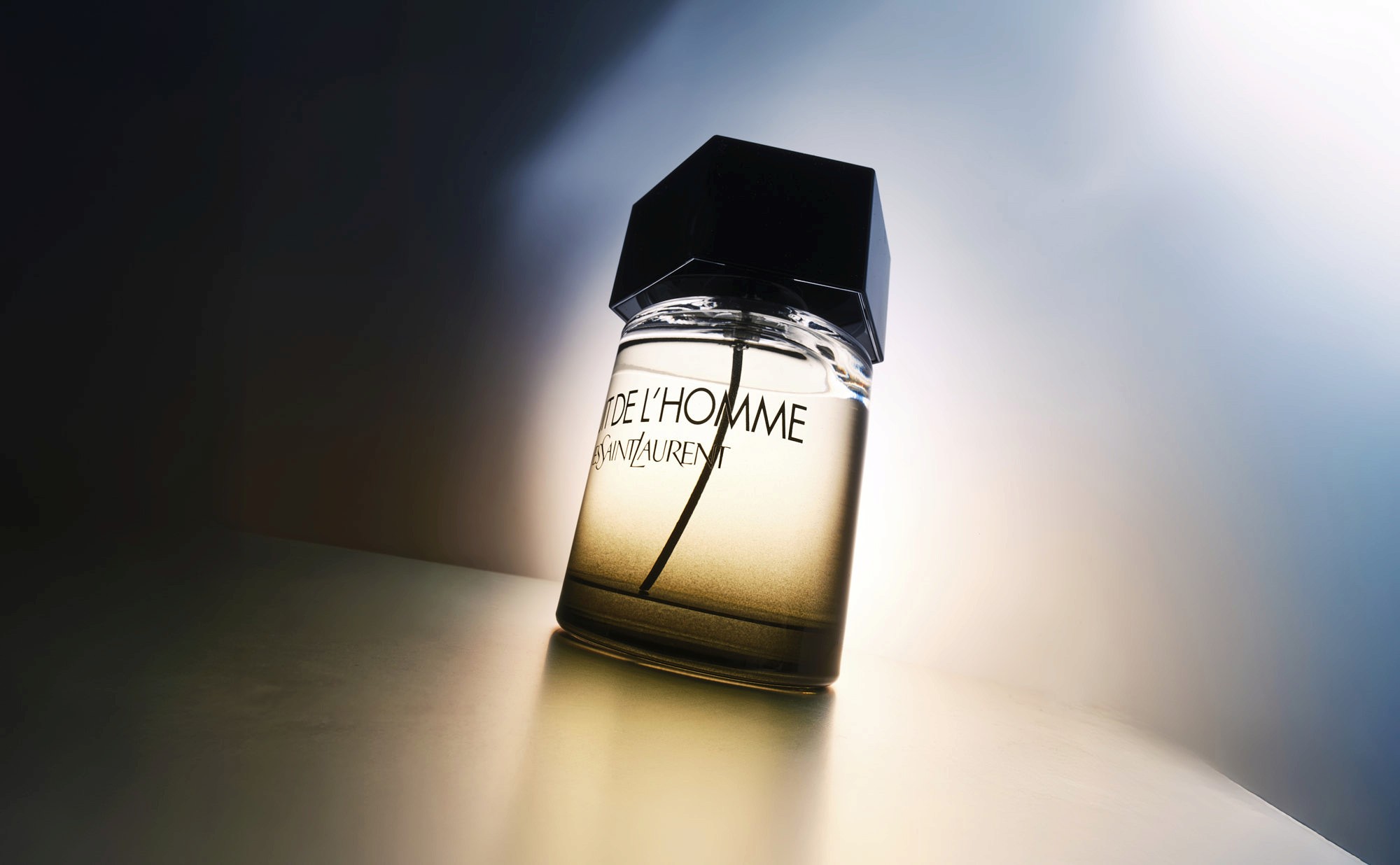 A perfume bottle is positioned at an angle, casting a warm light in a dimly lit space, creating a cozy atmosphere.