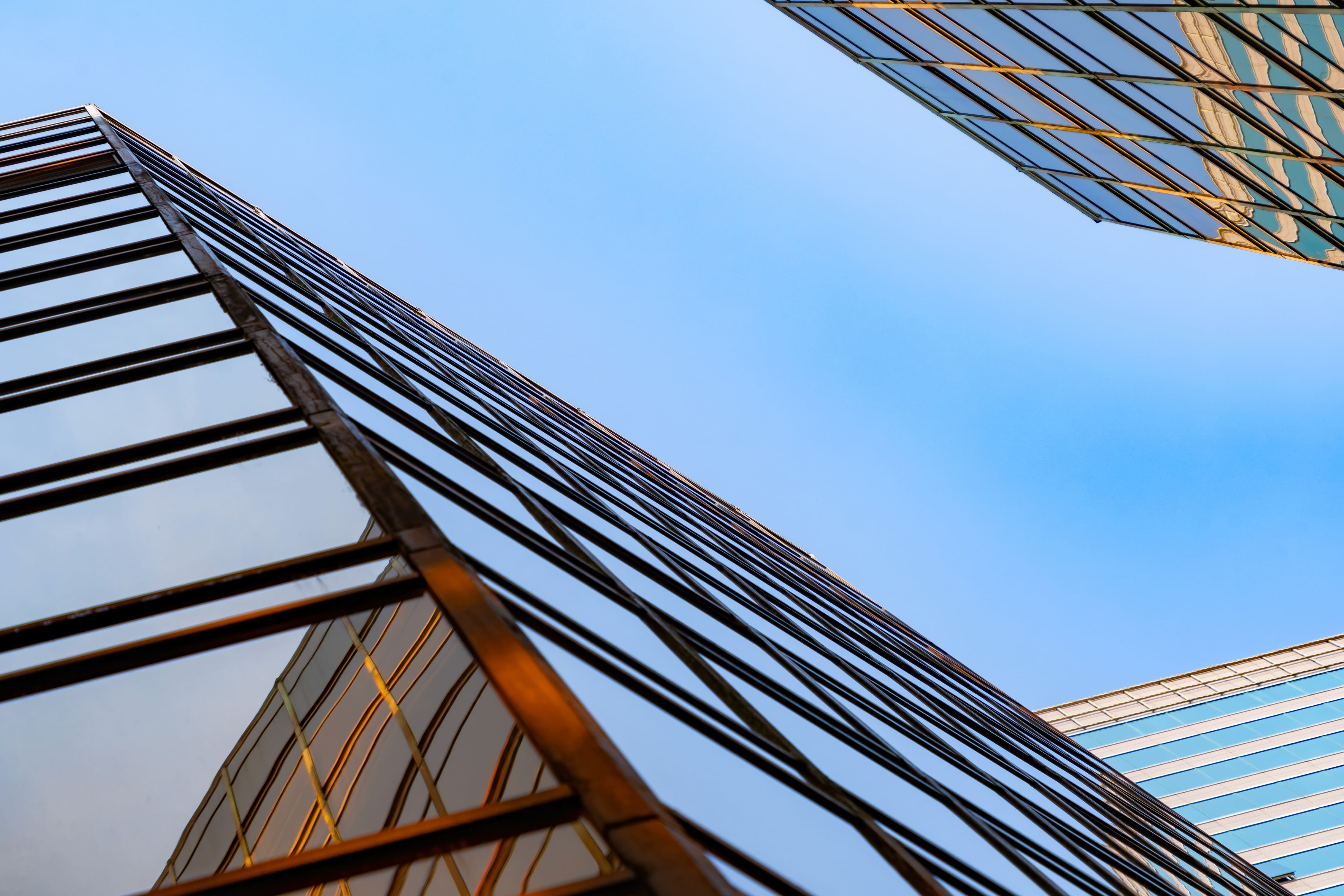 A low-angle view looking up at modern glass skyscrapers, their dark-framed windows reflecting golden sunset light against a clear blue sky.
