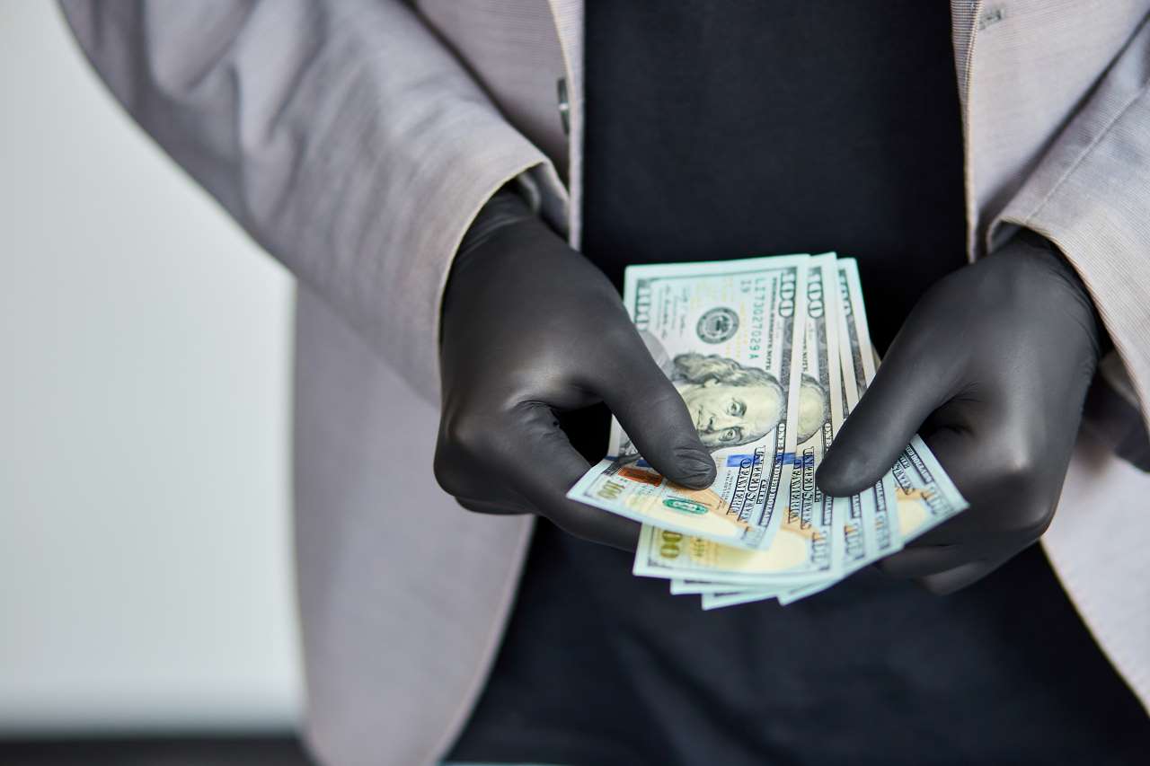 homem de luvas negras manuseando notas de dólar