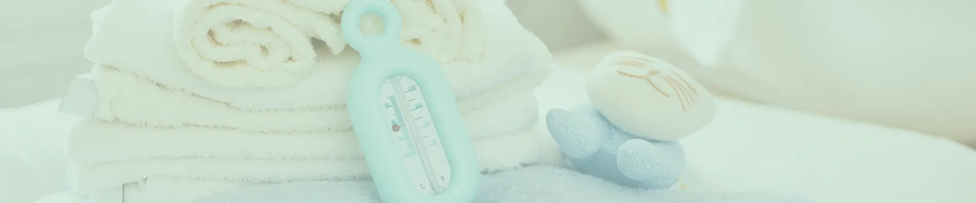 Stacked white towels with a blue bath thermometer and soft baby toy, highlighting gentle bath care for newborns.