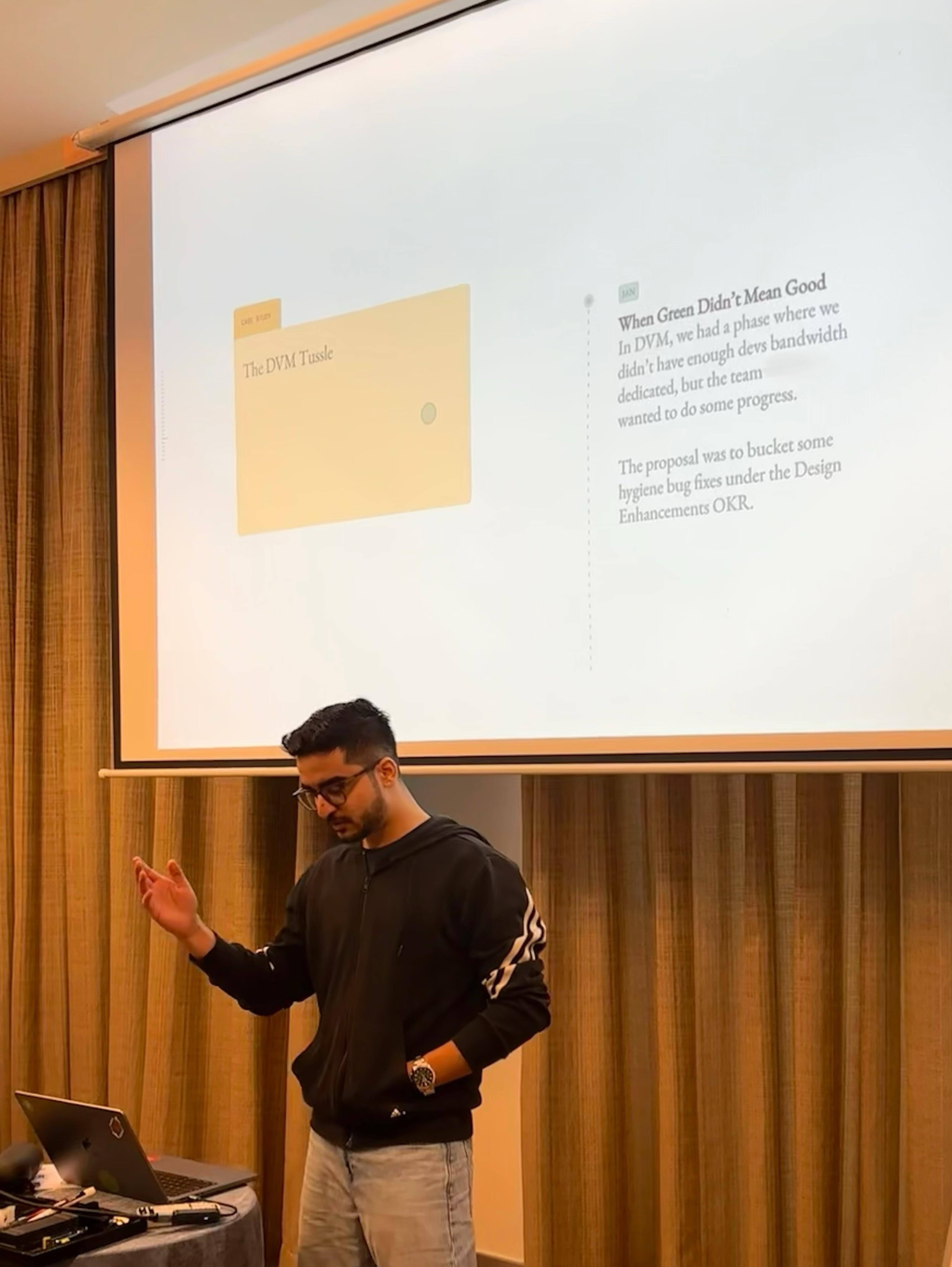 Una persona con una camiseta negra y pantalones de color claro está de pie en la cima rocosa de una montaña al atardecer, sosteniendo una cámara frente a su cara para tomar una foto. Un mar de nubes se extiende detrás de ellos, iluminado por la luz dorada del sol poniente.