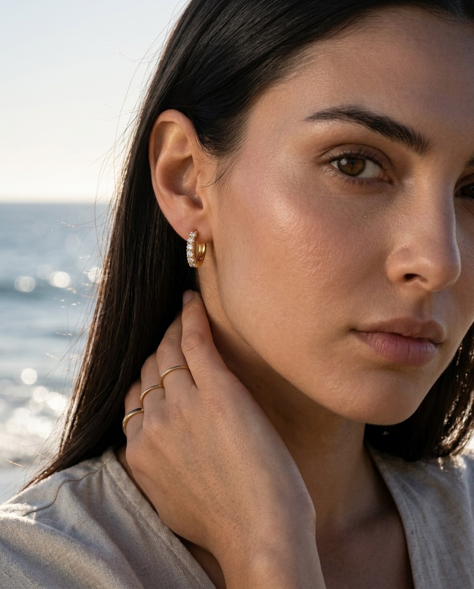 Tamar Buchnik AI model wearing gold huggie hoop earring and gold ring, coastal close-up editorial, natural daylight, Gemzy AI jewelry studio