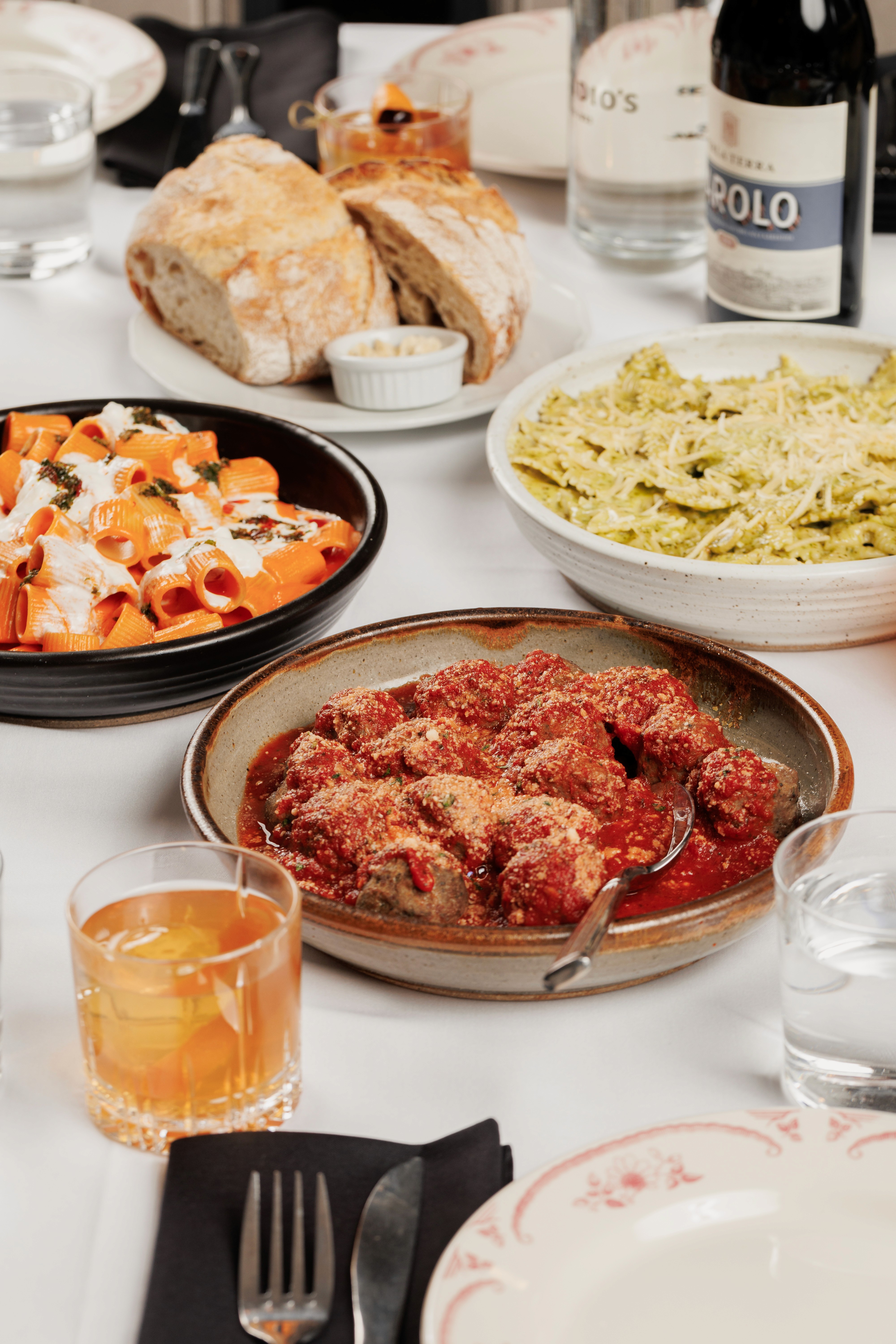 family style meal with meatballs, pesto pasta, rigatoni alla vodka and an old fashioned cocktail