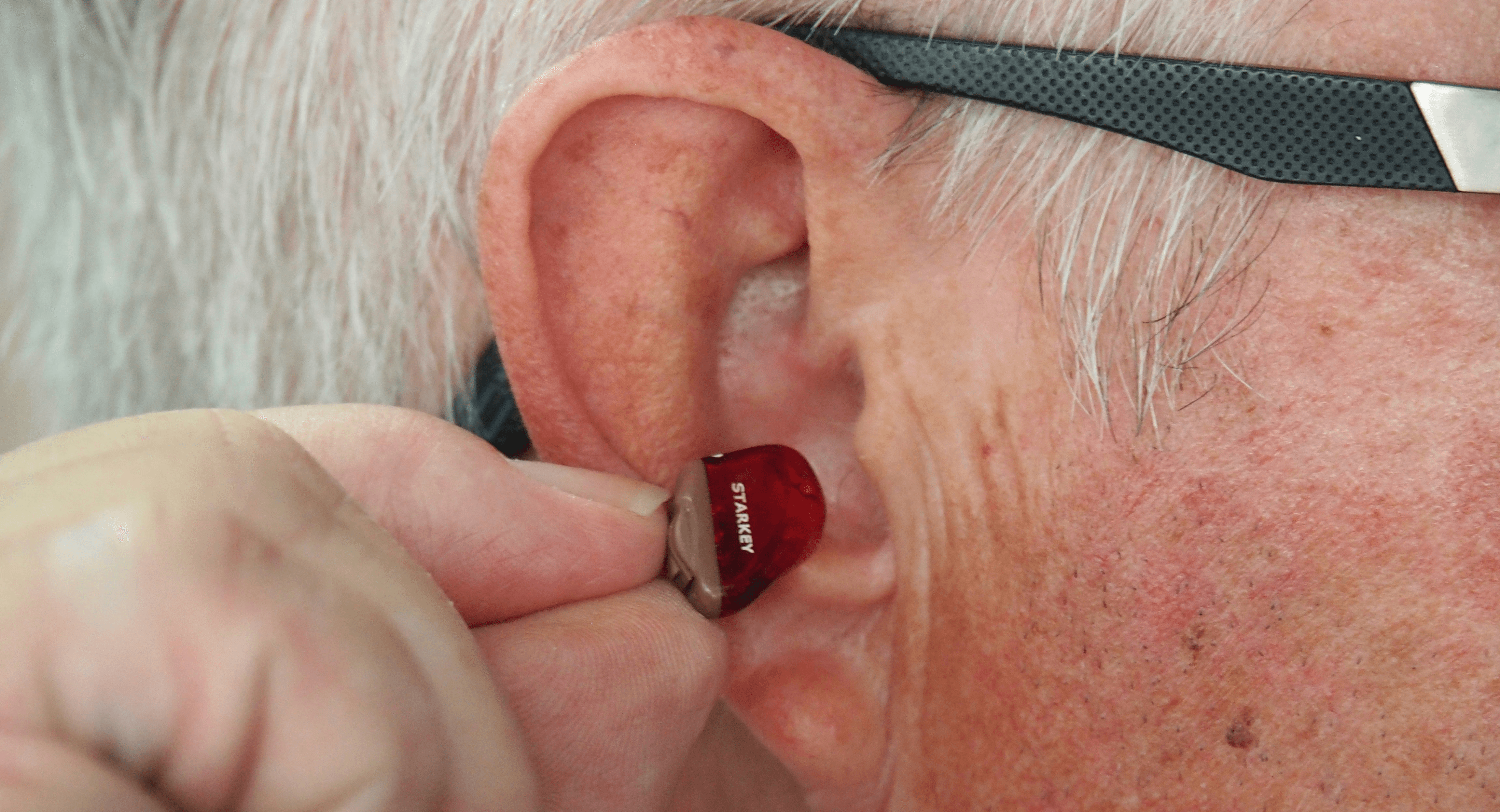 A close-up of a hand inserting a small device into an elderly person's ear.