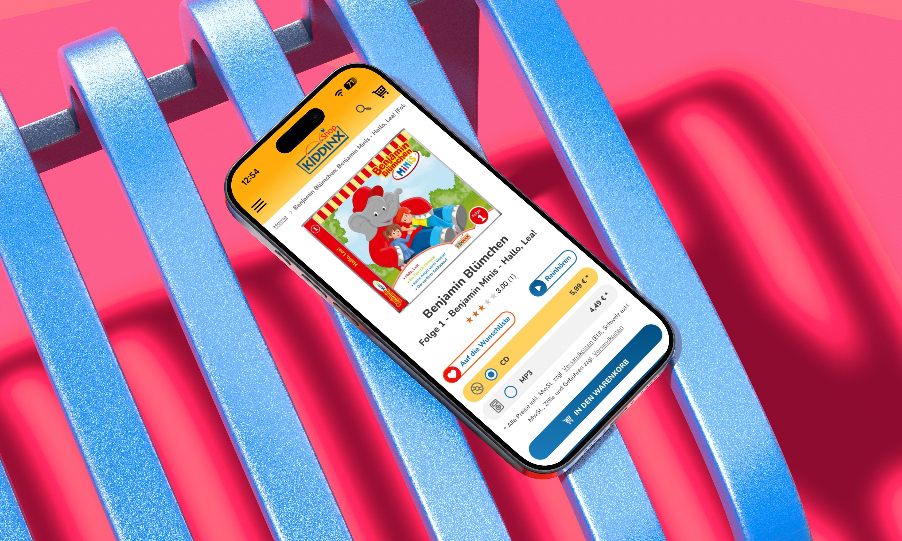 Smartphone mit geöffneter Kiddinx-App liegt auf pinkem Hintergrund mit blauen Streifen. Auf dem Bildschirm sind bunte Kinderinhalte zu sehen.
