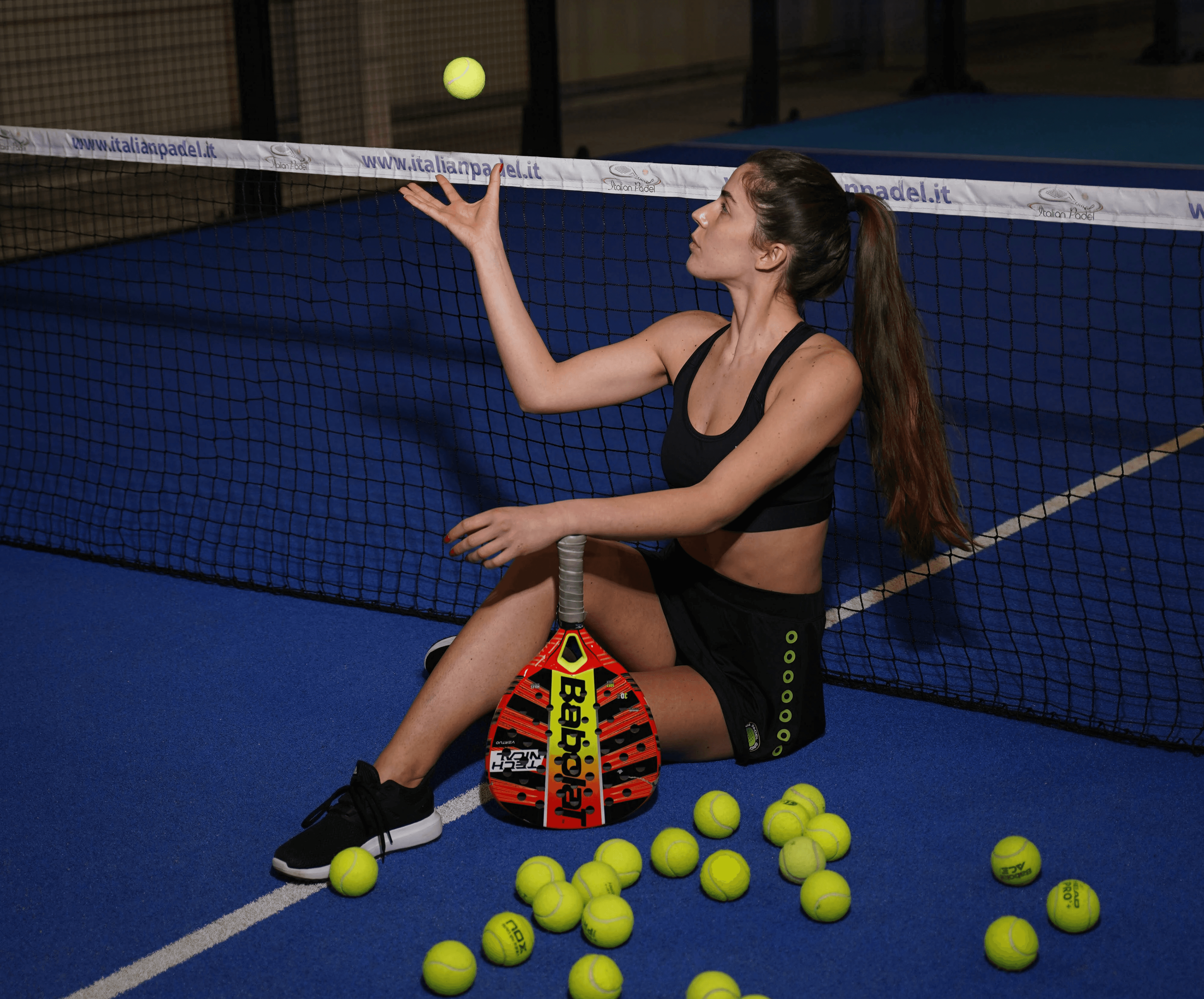 Woman sitting on padel court with tennis balls