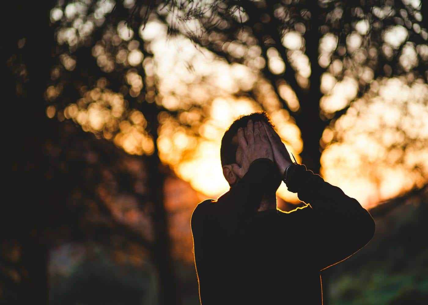 Man outside in nature covering his face with his hands to showcase physical burnout