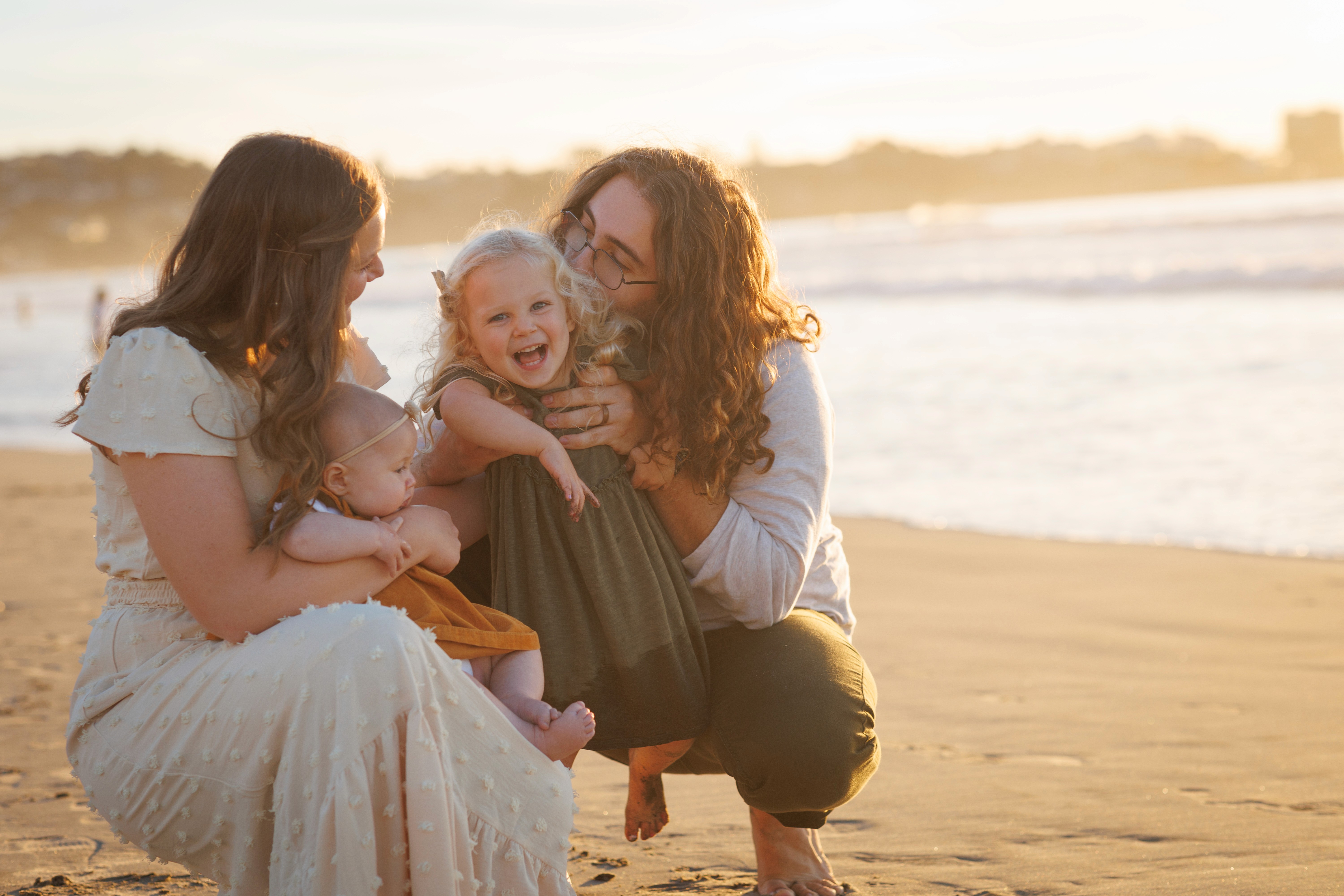 Parents sitting on the sand with children, laughing together during a family beach session in San Diego.