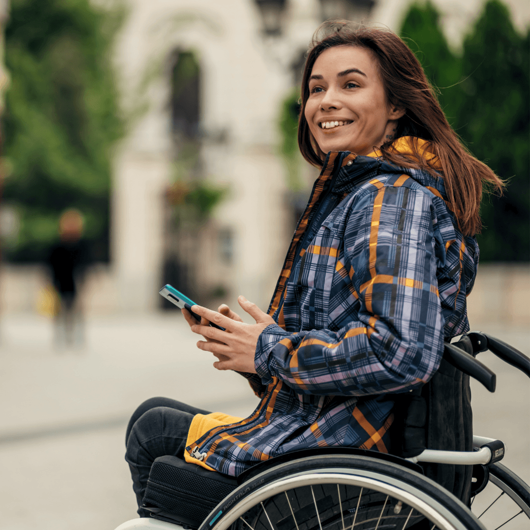 A woman in a wheelchare holding her phone in front of a cafe