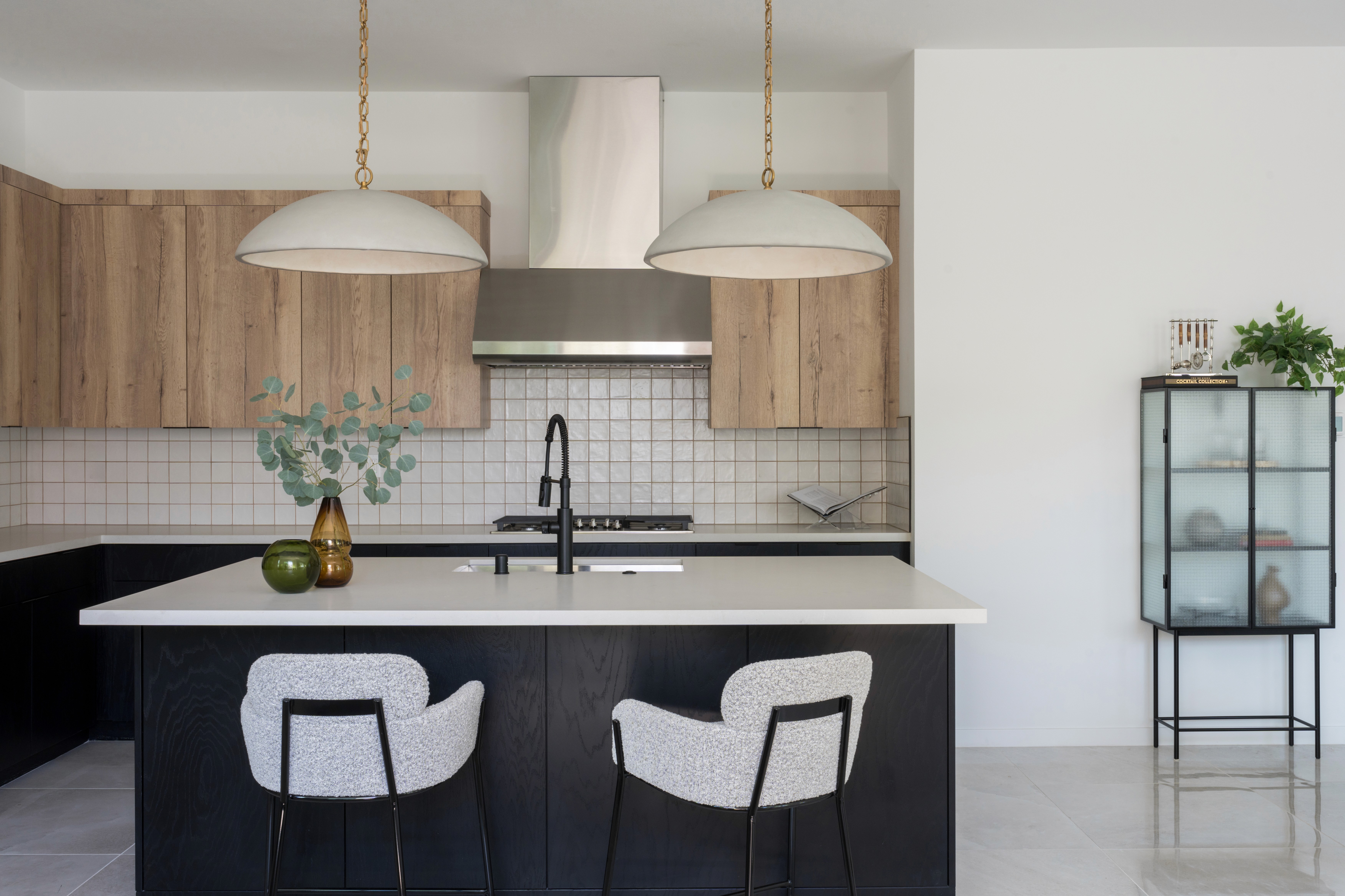 Modern kitchen island with dark wood panels, white countertops, grey barstools, white pendant lighting with gold accents and cool toned cabinetry by Jubilee Interiors in Arcadia, California