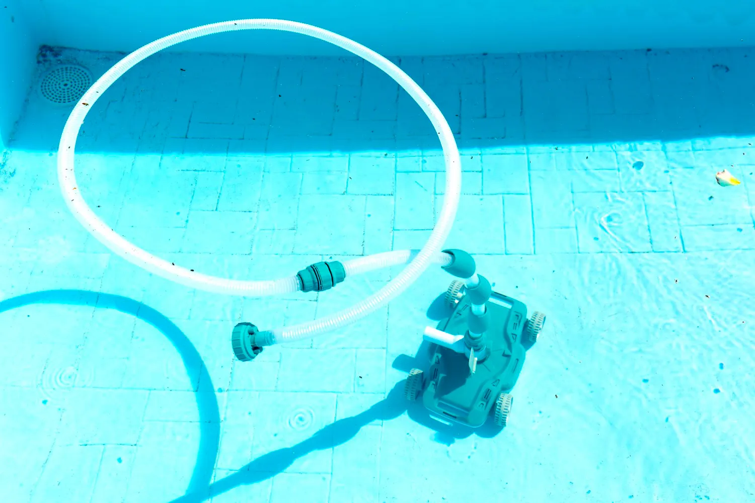 Automatic pool cleaner with a long hose operating on the floor of a light-blue residential pool.
