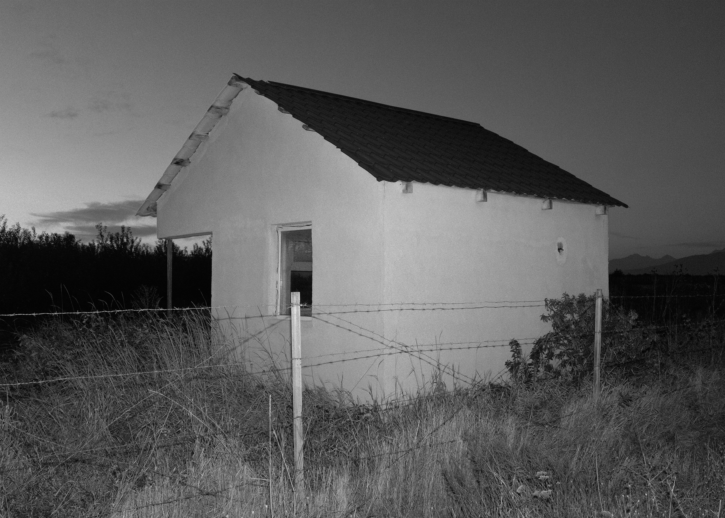 An abandoned house behind a barbed-wire fence.