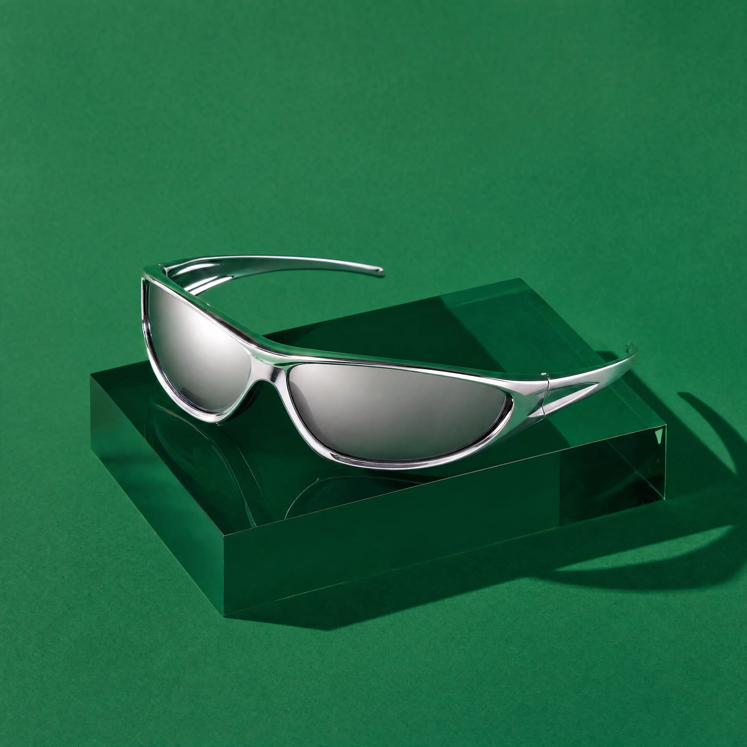 Chrome wraparound Ferro sunglasses on a green acrylic block against green