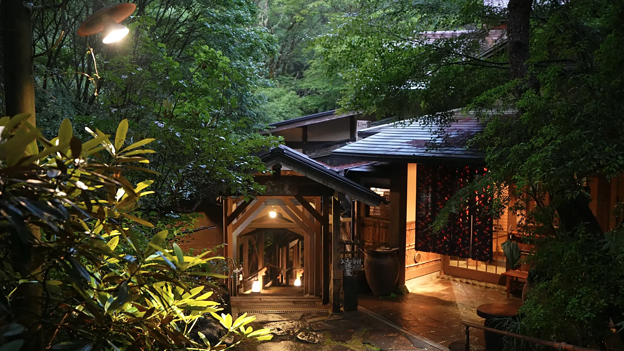 A lit inn entrance at Kurokawa Onsen at dusk under a timber portico