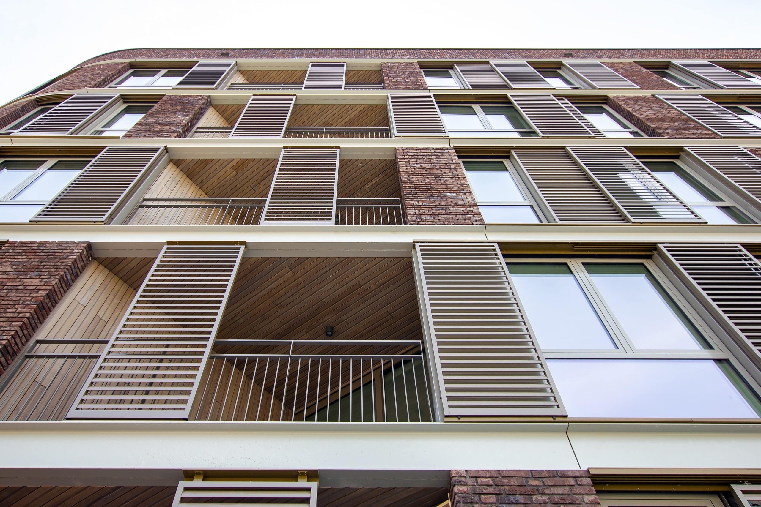 Gezicht op hoog bakstenen gebouw met balkons voorzien van lamellen en relingen.