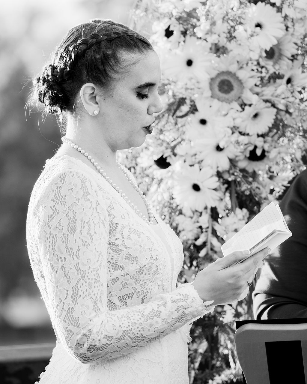 Novia con vestido de encaje leyendo sus votos junto a un muro de flores