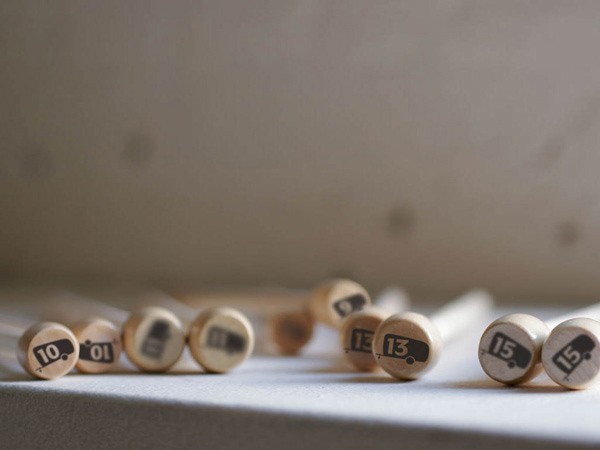 Several wooden dowels with numbered markings are arranged on a light-colored surface. The numbers visible are 10, 10, 13, 15, and 15. The background is a light gray wall with subtle texture.