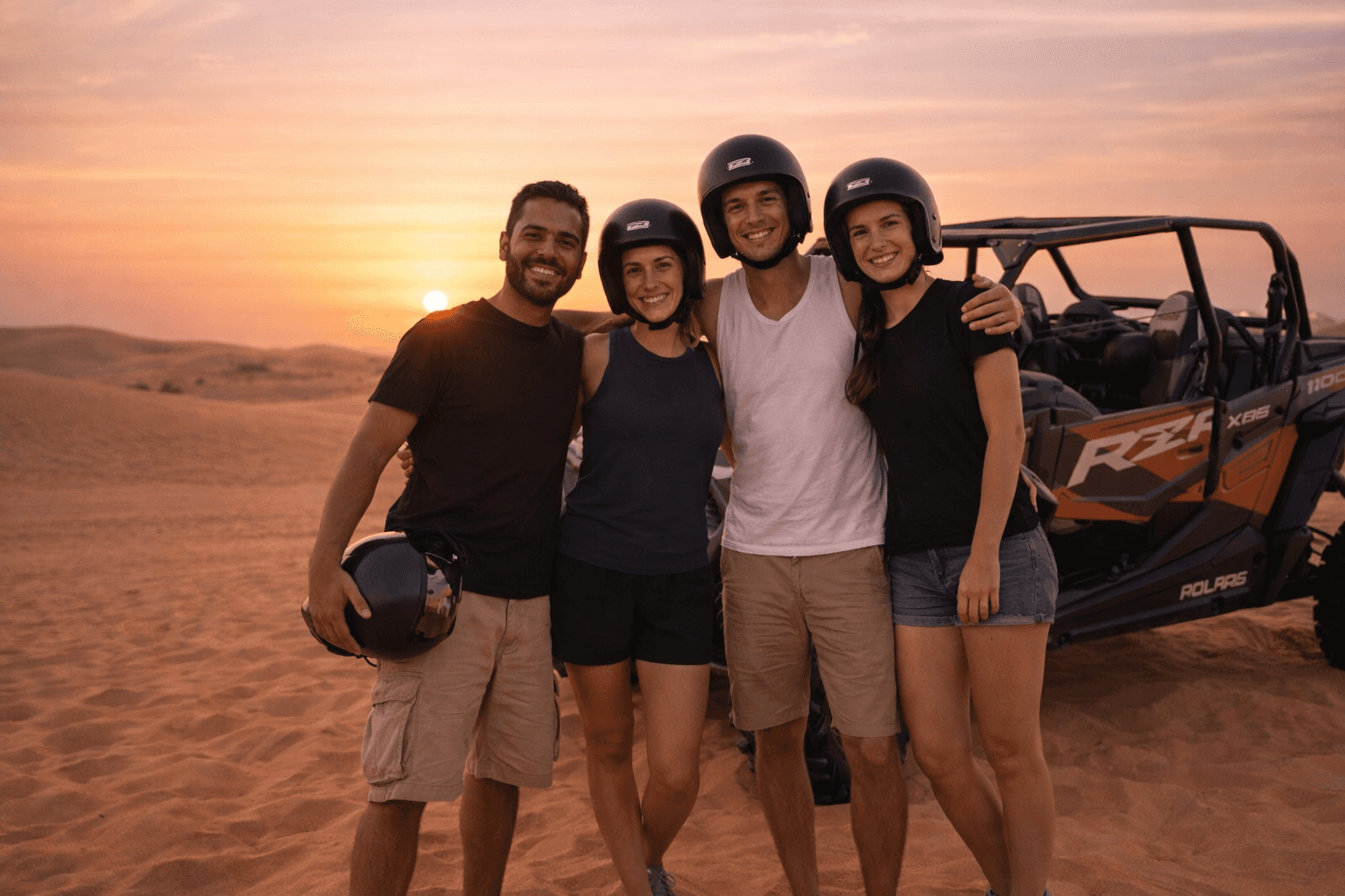 A group of friends smiling at sunset during a Polaris RZR buggy tour in the Dubai desert with Dune Quest Tours