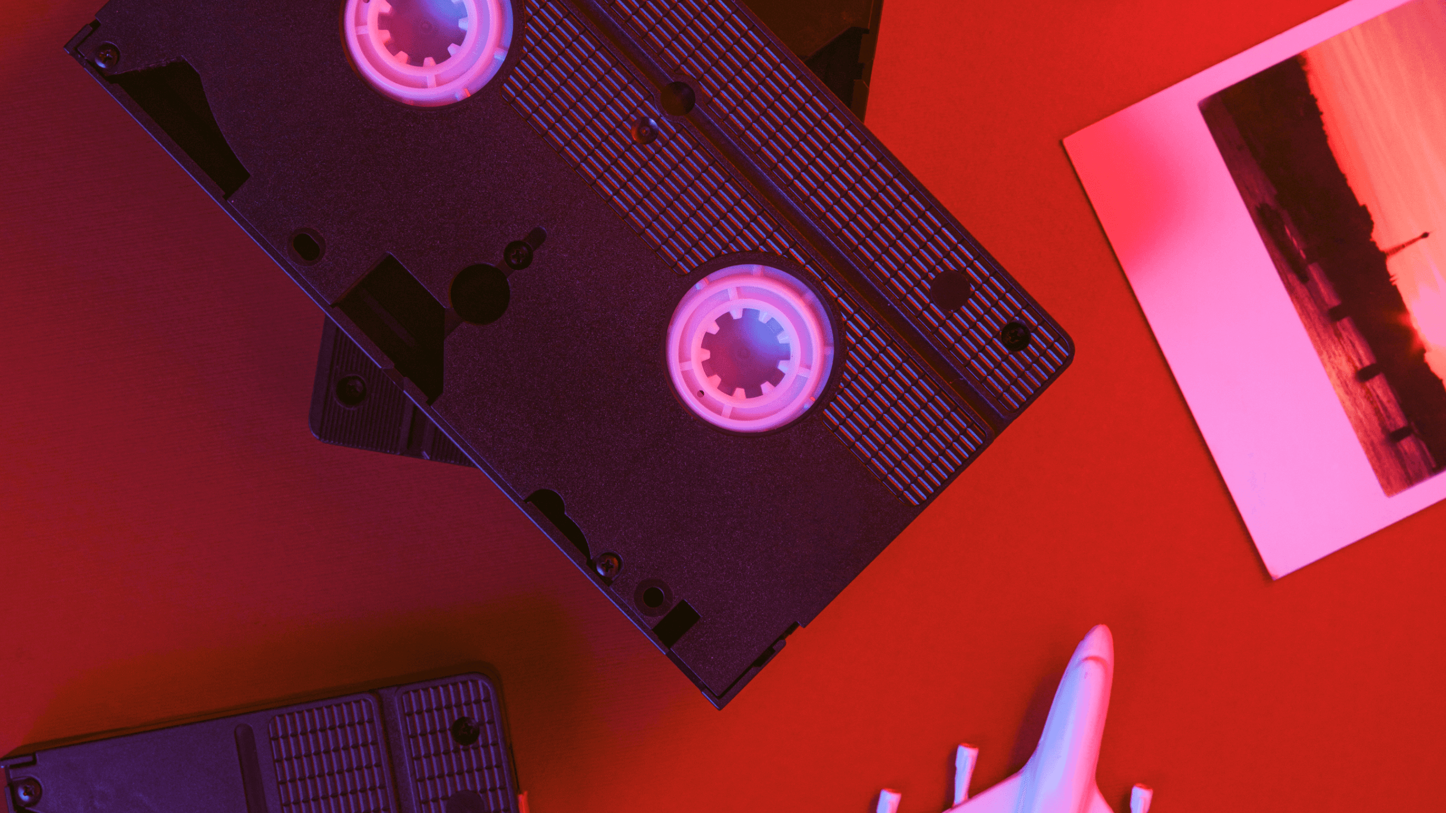 Retro VHS tapes and a photo on a red surface under pink lighting.