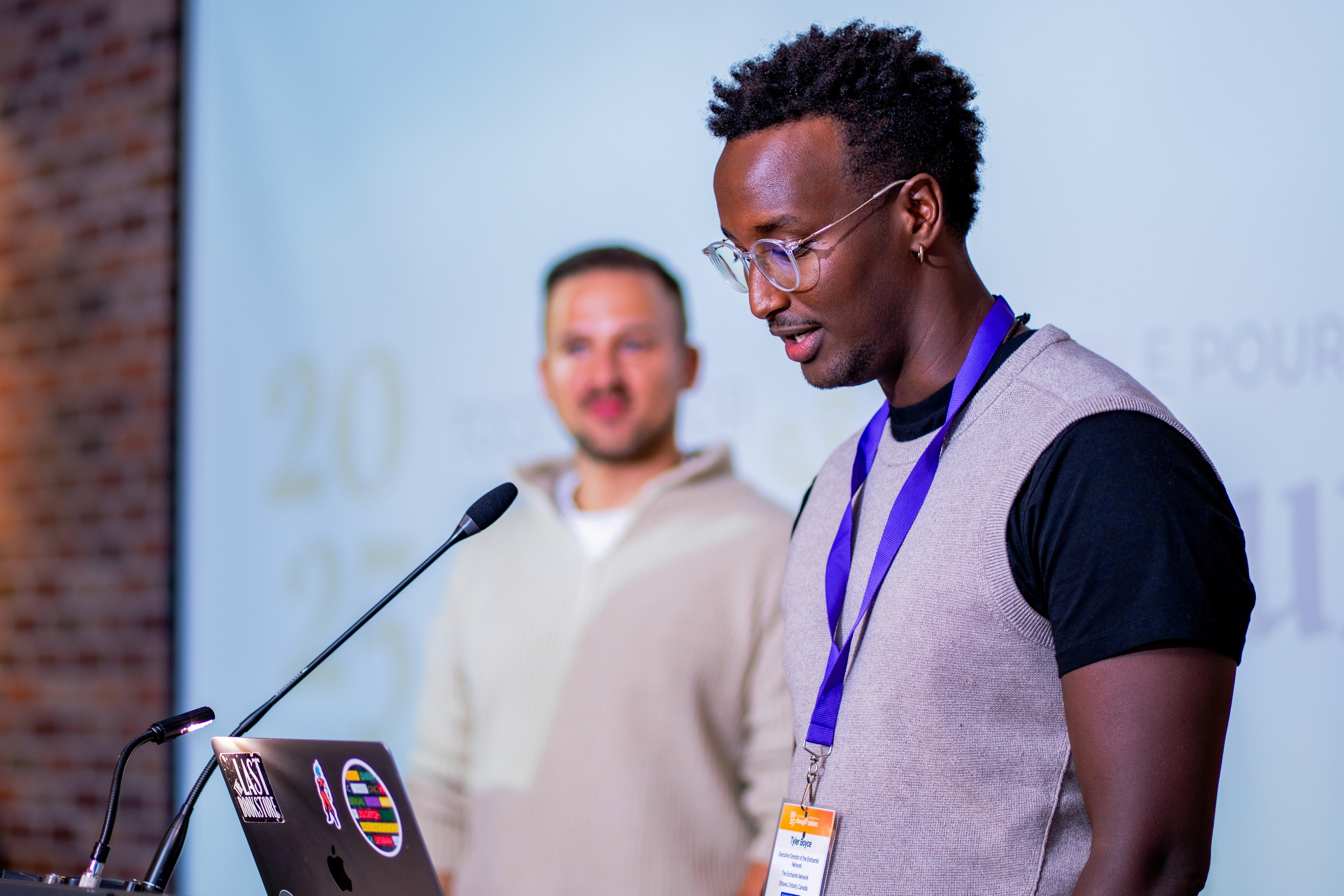 Three individuals stand in a dimly lit room with purple lighting, engaged in conversation or listening intently.