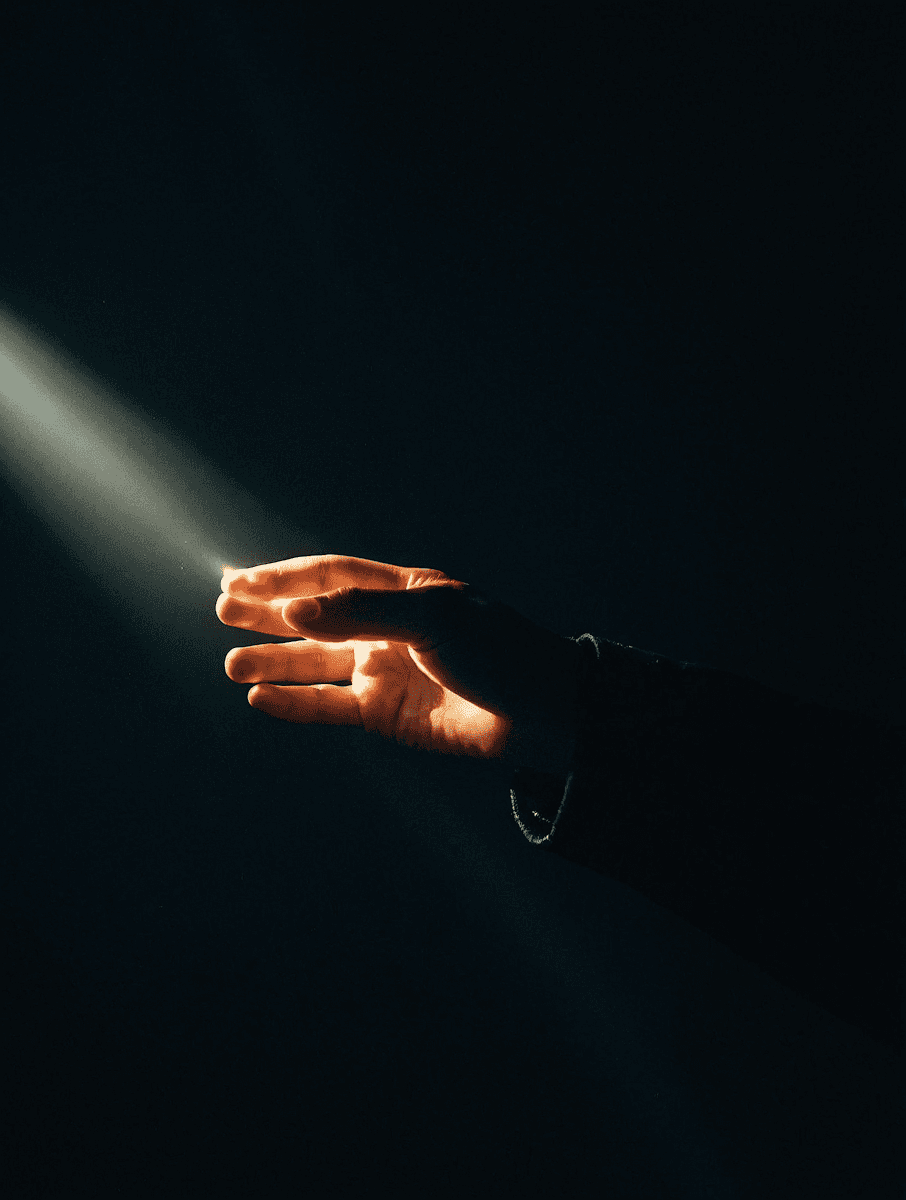 A hand reaches into a beam of light in a dark setting, creating a dramatic and serene contrast. Perfect for themes of hope or introspection.