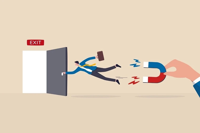 A businessman in a suit and tie, holding a briefcase, is about to exit a door labeled "EXIT." A hand from the outside is holding a large magnet, pulling the man away from the exit door.