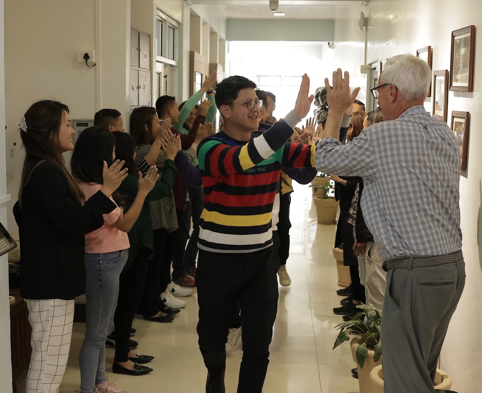 A group of people clapping and giving high fives in a hallway, celebrating with smiles and raised hands.