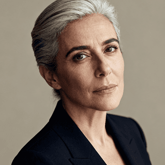 A woman with gray hair wearing a black suit, standing confidently with a neutral expression.