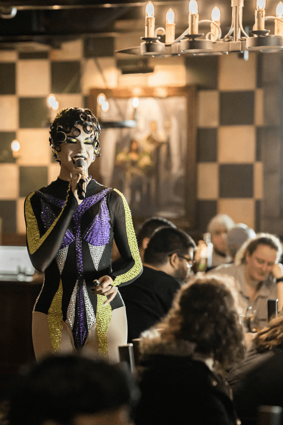 Drag queen Trinket estrange in tavern hosting trivia with microphone