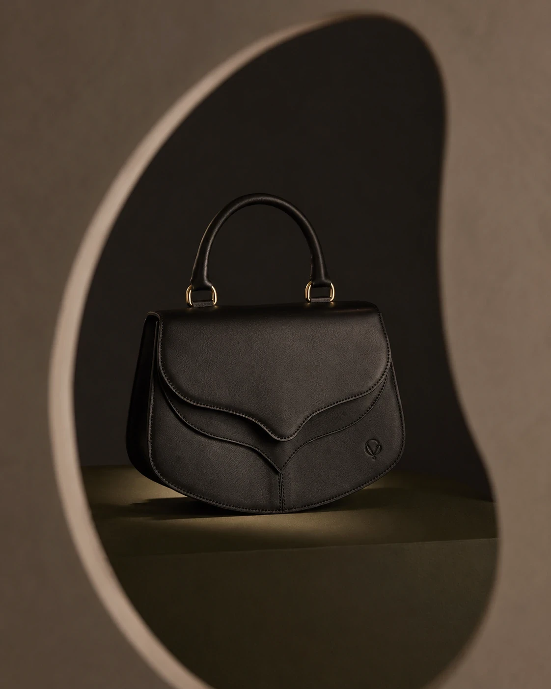 Black leather handbag inside a softly lit architectural niche.