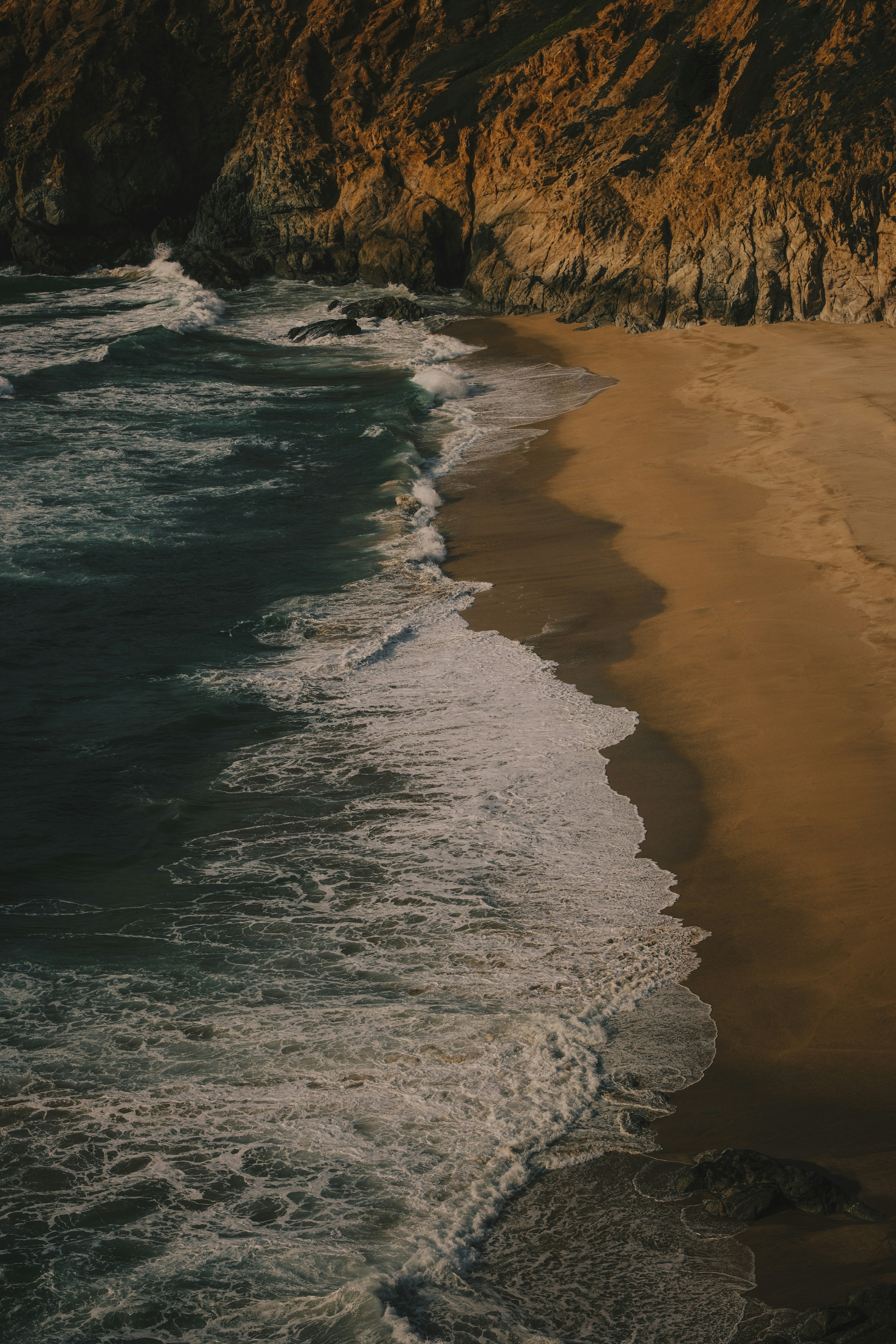 Waves crash on a sandy beach next to cliffs.